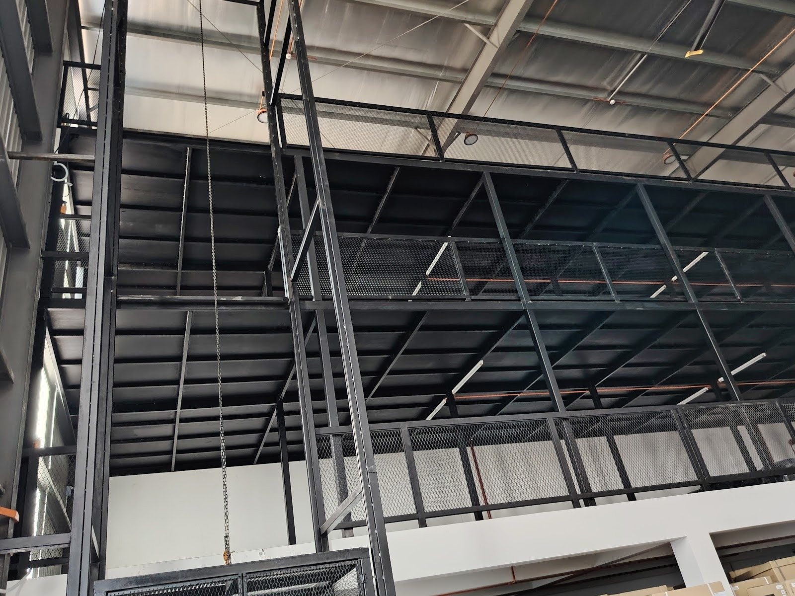 Steel I-beam mezzanine structure with mesh railing inside a warehouse